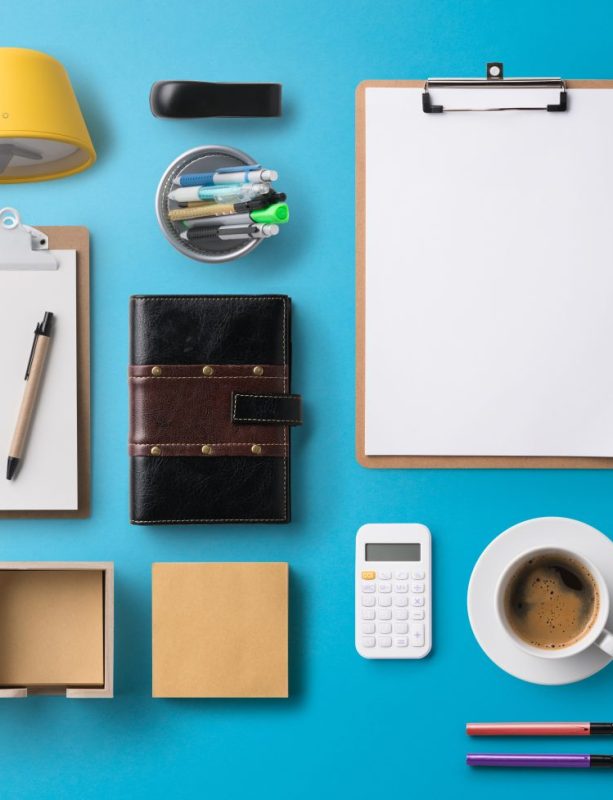 Flat lay top view office desk working space with laptop, tablet, smartphone and supplies on blue background.
