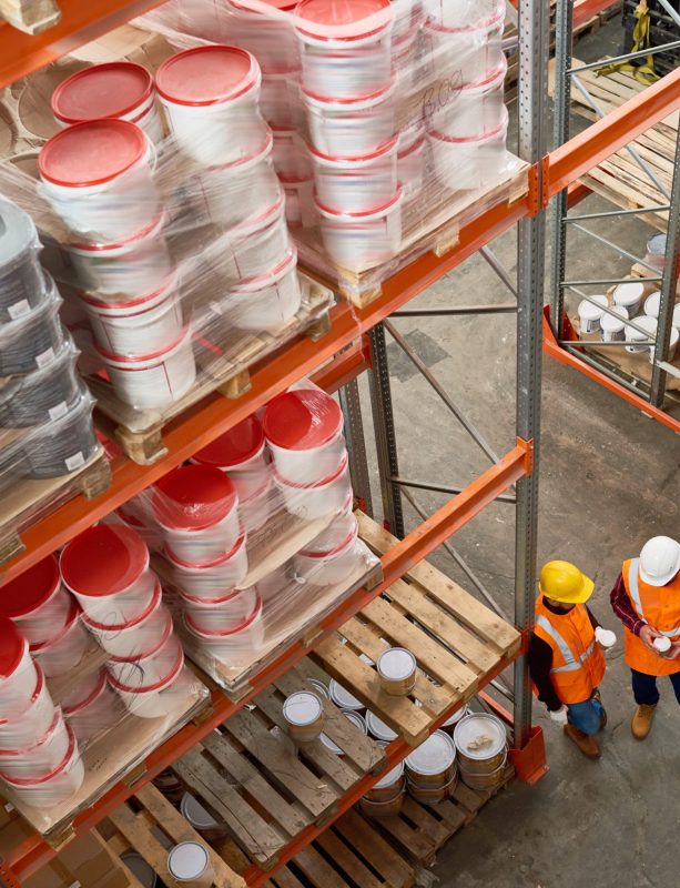 High angle  background image of tall shelves in modern warehouse with two workers wearing hardhats standing in aisle, copy space